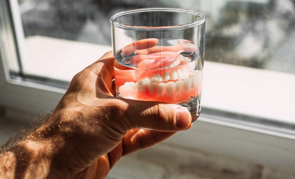 Man holding a glass of water with dentures soaking inside of it