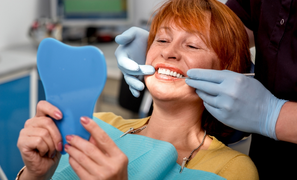 Redheaded woman looking at her smile in mirror in dental chair