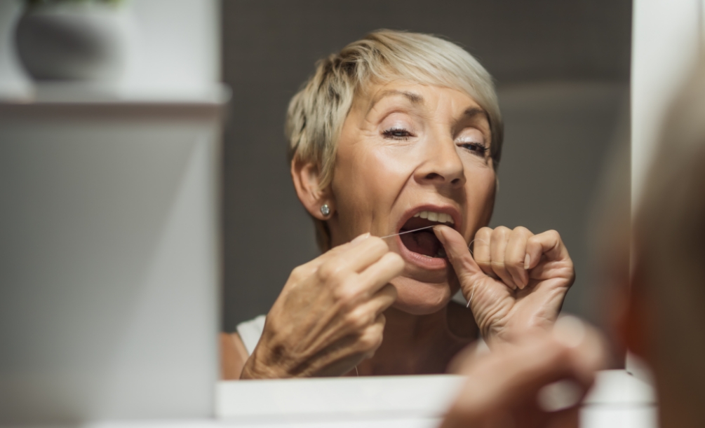 Older woman flossing in front of mirror