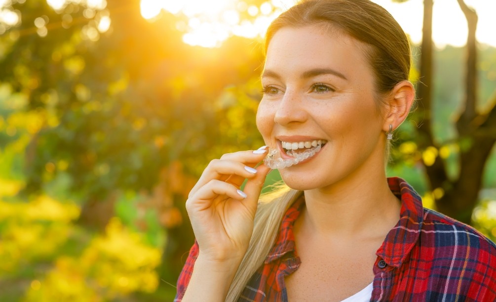 Young woman outdoors placing Invisalign aligner over her teeth