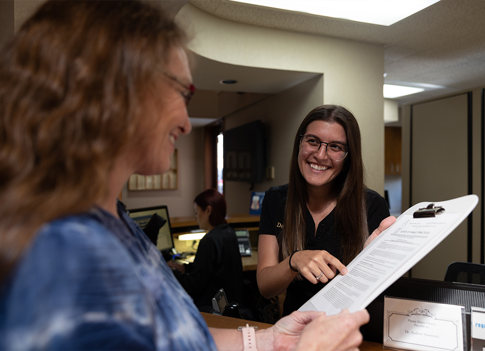 Dental team member showing a patient where to sign on paper on clipboard