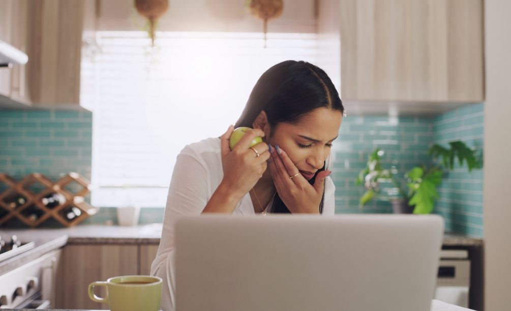 Woman sitting at table holding apple in one hand and her cheek in the other