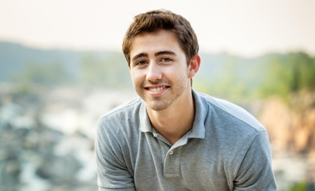 Young man in gray polo shirt smiling outdoors