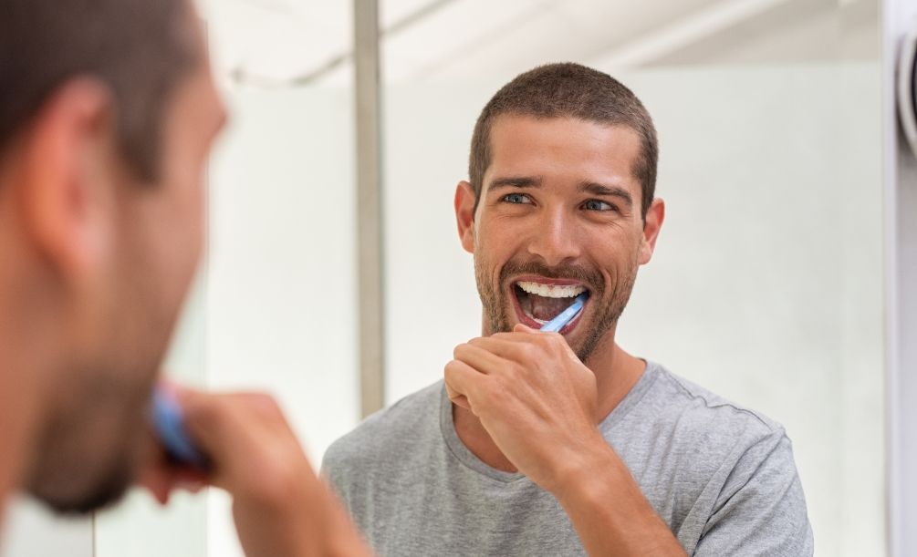 Man in gray tee shirt brushing his teeth