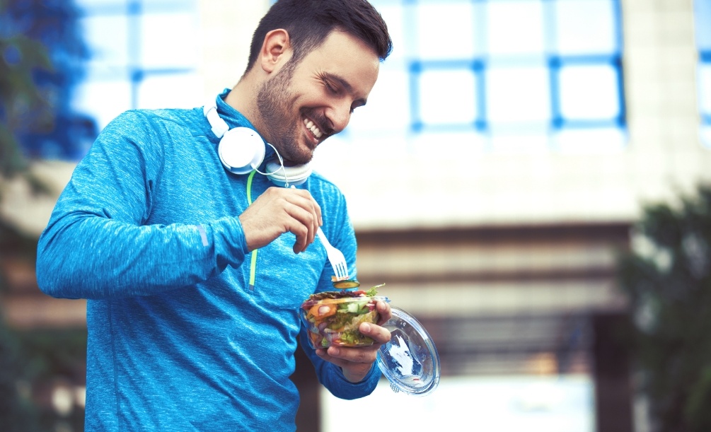Man in jogging clothes eating salad while standing outdoors