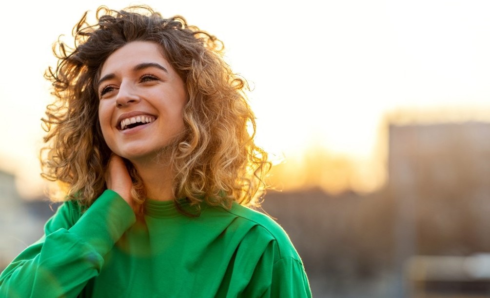 Young woman in green sweater grinning outdoors on sunny day