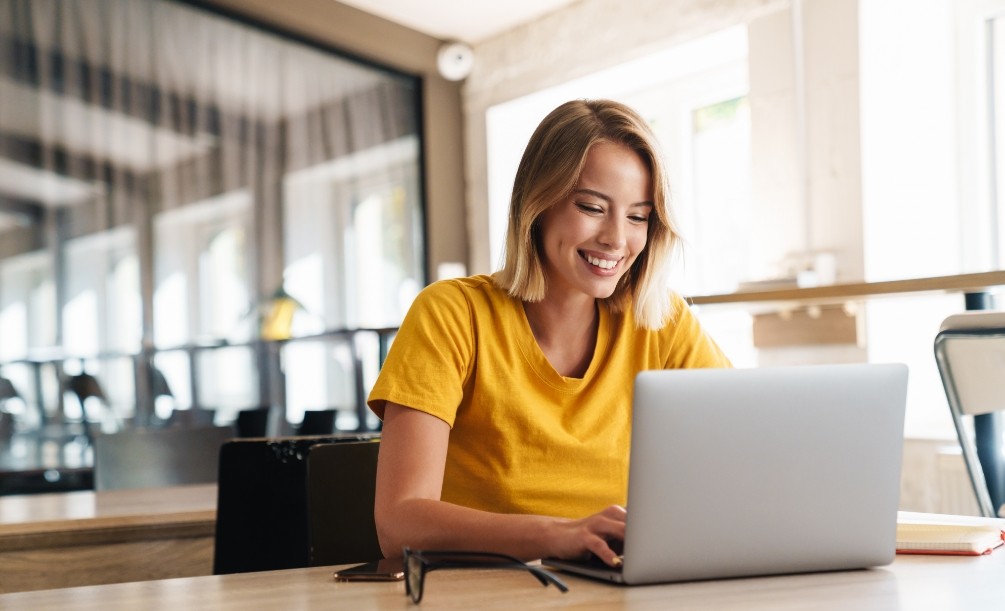 Smiling woman in yellow T shirt typing on laptop