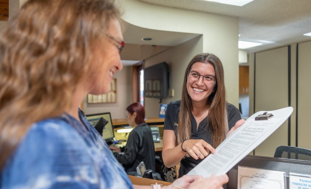 Dental team member pointing to a form on clipboard while talking to a patient