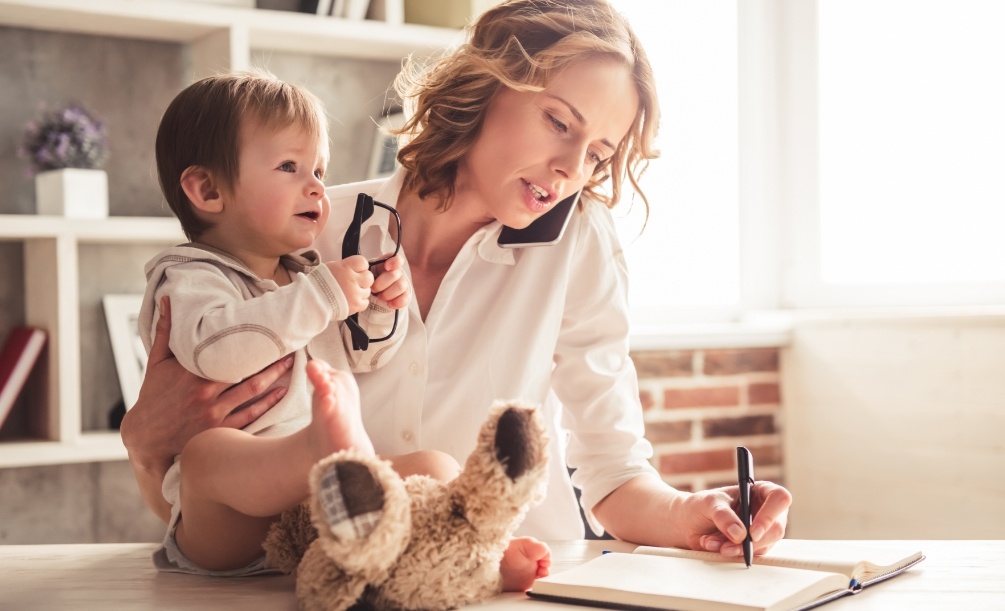 Woman completing paperwork while holding her baby in her other arm