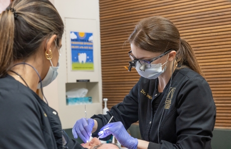 Two dental team members wearing protective gear while treating a patient