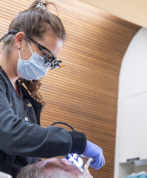 Dental team member shining a light into the mouth of a patient during dental procedure