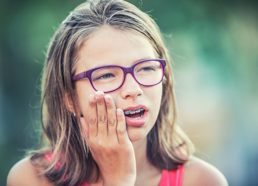 Teenage girl with braces holding her cheek in pain