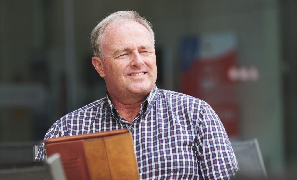 Older man in black and white plaid shirt sitting in front of a window