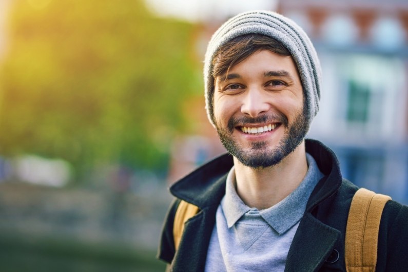 Young man in gray beanie smiling outdoors