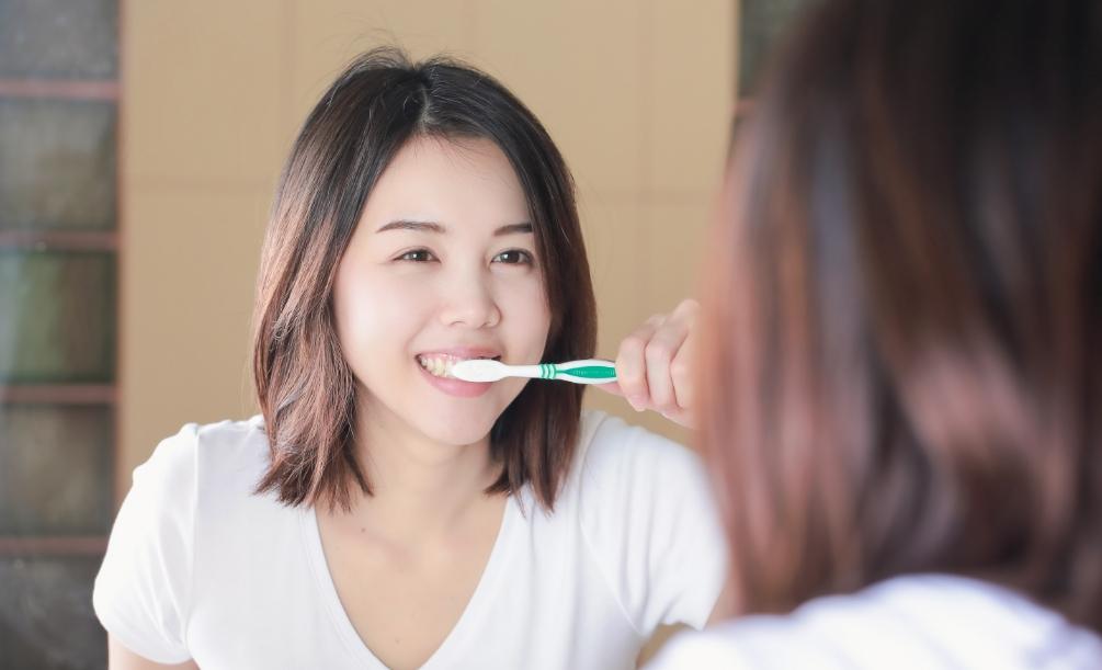 Woman brushing her teeth in front of bathroom mirror