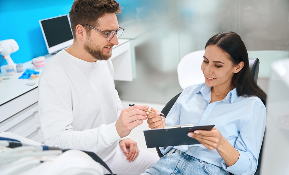 Man in white handing pen to patient in dental chair to fill out forms